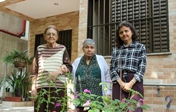 Três senhoras em frente a um jardim. São integrantes da Comunidade Irmã Ivone Drummond.