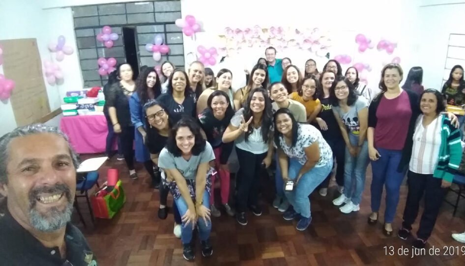 Grupo grande de pessoas em uma confraternização, com balões rosa espalhados pelas paredes.