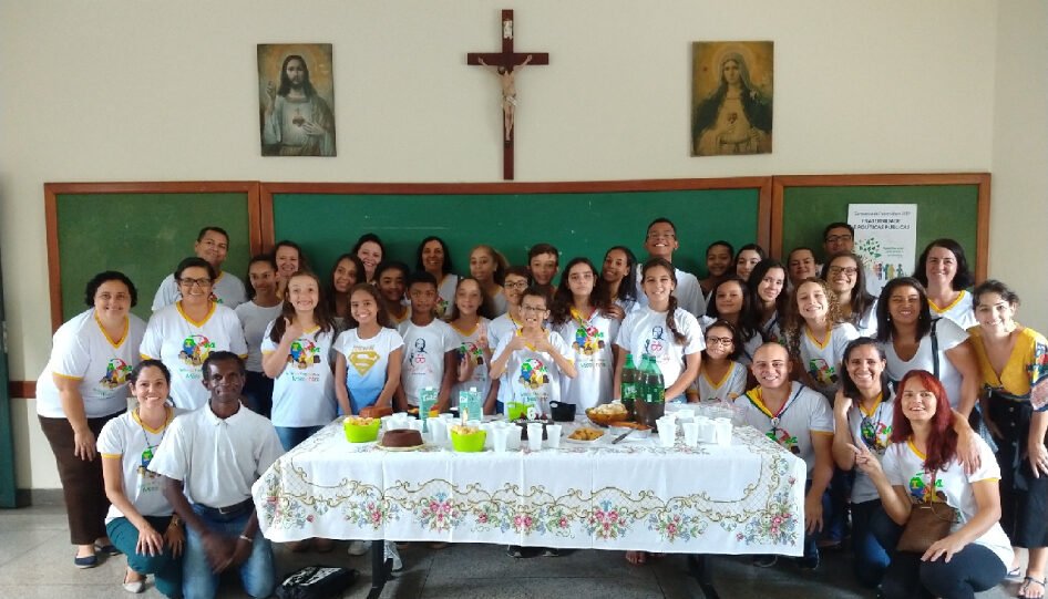 Grupo de pessoas em uma sala de aula, em frente a uma mesa com bolos.