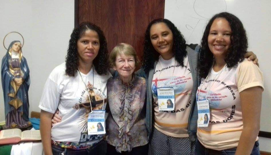 Quatro mulheres abraçadas ao lado de uma santa.