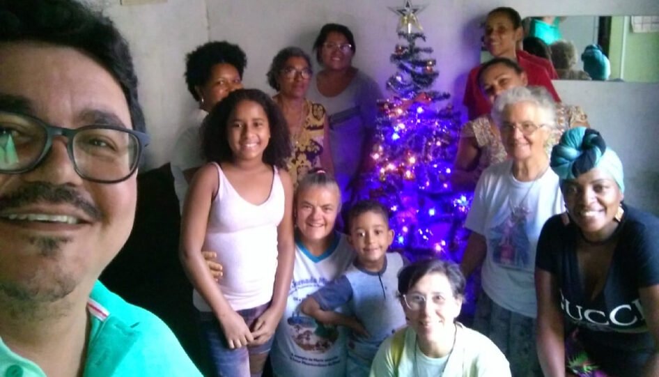 Doze pessoas em uma sala. Dentre elas, há uma árvore de Natal, decorada.