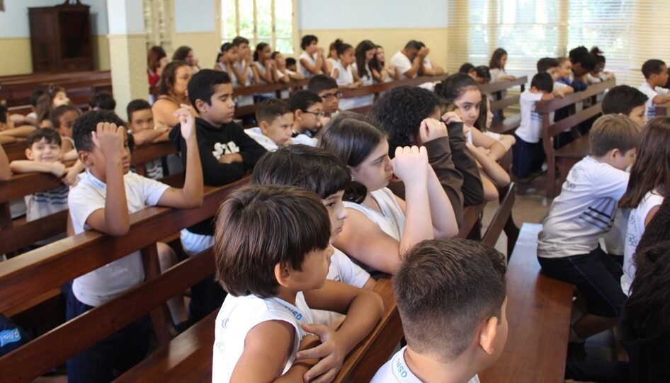 Grupo de crianças ajoelhada em bancos de igreja.