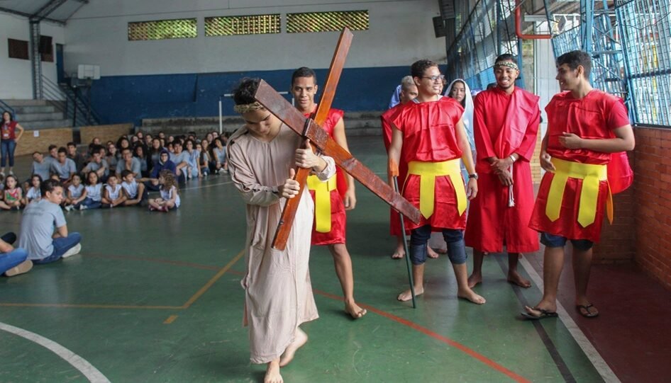 Adolescentes participando de uma peça de teatro. O da frente carrega uma cruz.