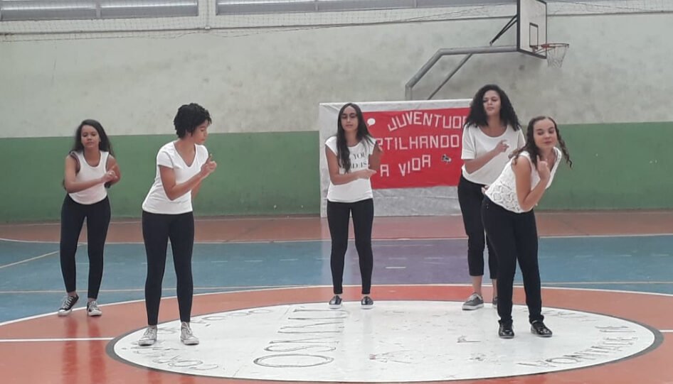 Cinco adolescentes dançando em uma quadra.